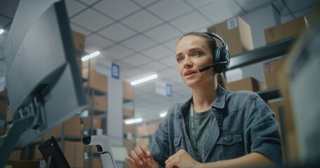 Female logistics manager in headset talks on call with customer, uses computer. Sorting center...
