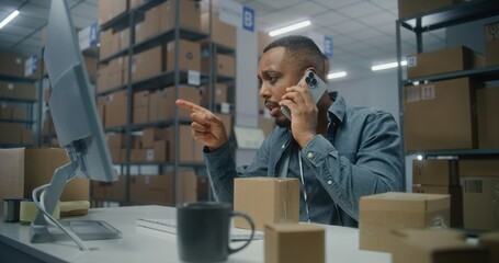 Sorting center: Male African American warehouse associate talks to customer by mobile phone, checks...