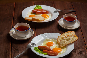Breakfast two plates fried eggs with sausages white bread and tea in cups