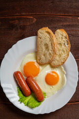 Breakfast fried eggs with sausages crispy white bread and tea in a cup on a wooden table