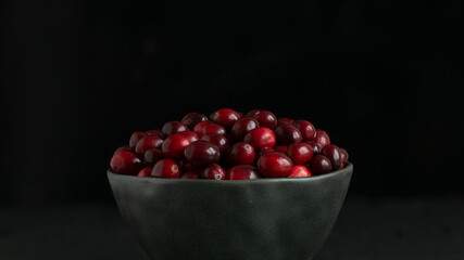 red cranberries lie with slide in black ceramic bowl on black background