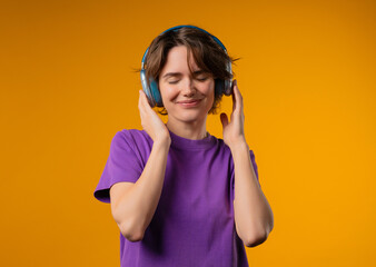 Joyful woman listening music in vibrant yellow studio, headphones on, fully immersed in. Her energy...