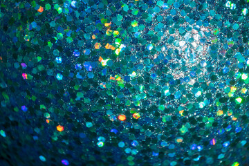 A close-up of a glittering blue surface, featuring hexagonal reflective particles with iridescent...