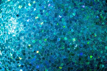A close-up of a glittering blue surface, featuring hexagonal reflective particles with iridescent...