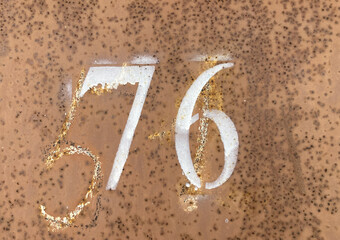White number 76 on aged background. Seventy-six on textured rusty surface