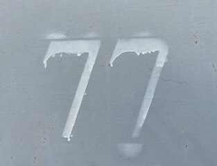 White number 77 on aged background. Seventy-seven on textured surface 