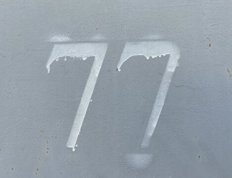 White number 77 on aged background. Seventy-seven on textured surface 