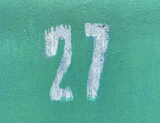 White number 27 on aged turquoise background. Twenty-seven on textured surface with old paint