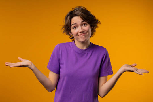 Confused pretty woman, shoulders up - can't help, makes gesture of I dont know. Difficult question, guilty reaction, puzzled stylish lady on yellow background