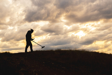 A man is walking on a hill with a metal detector in his hand