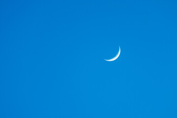 A crescent moon is flying through a clear blue sky