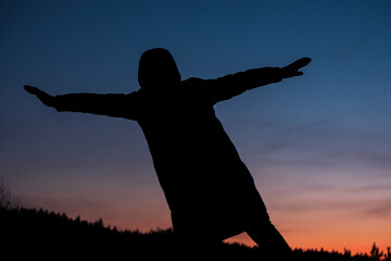A silhouette of a person is shown in the sky at sunset