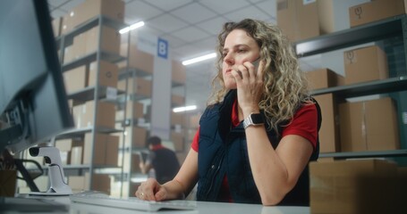Warehouse facility of post office or E-commerce store: Female logistics coordinator talks by mobile...