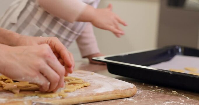 mother and little child daughter baking Christmas cookies from dough in kitchen. close up