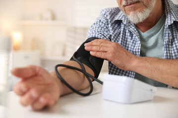 Senior man measuring blood pressure at table indoors, closeup