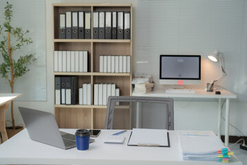 Office desk featuring a laptop displaying accounting documents, a calculator, stationery, a desktop computer, ring binders, a desk lamp, coffee cup, and smartphone, creating a productive workspace