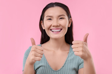 Woman with beautiful nose showing thumbs up on pink background. Rhinoplasty surgery