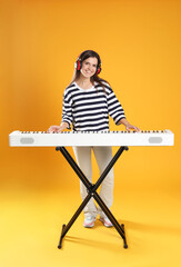 Smiling woman in headphones playing synthesizer on orange background