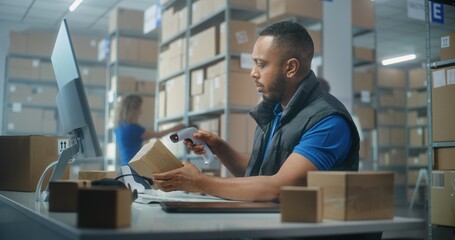 African American post office employee scans cardboard parcel using barcode scanner, works on computer. Sorting center workers carrying boxes for delivery to clients. Online E-commerce shop warehouse.