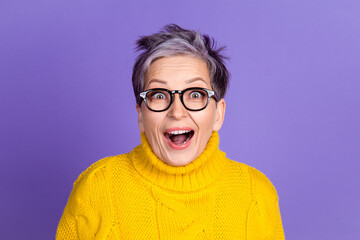 Happy woman with glasses expressing surprise in bright yellow sweater against purple background