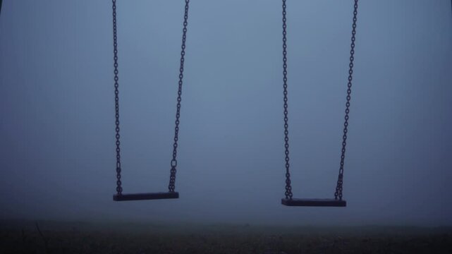 Children swings in eerie dark foggy playground