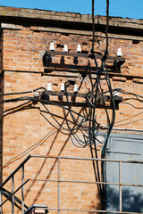 Brick building with tangled electrical wires, cables, and industrial elements under sunlight