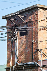 Brick building with tangled electrical wires, cables, and industrial elements under sunlight
