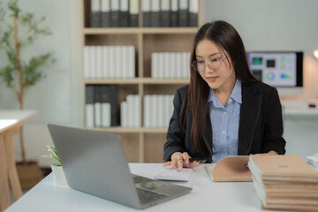 Businesswoman using calculator and working on laptop computer, managing company accounting documents and working on business project in office