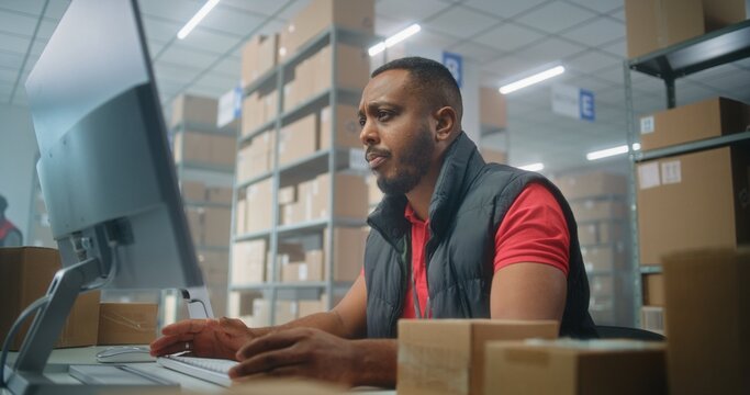 African American post office employee scans cardboard parcel using barcode scanner, works on computer. Sorting center workers carrying boxes for delivery to clients. Online shop warehouse. Slow motion