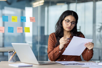 Serious focused woman behind paperwork reviewing analyzing and checking financial reports,...