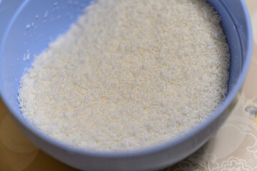 Shredded coconut close-up in a plastic blue bowl.
