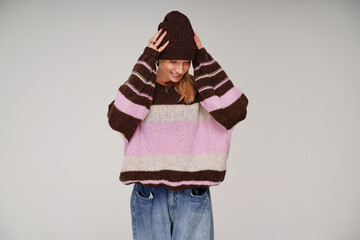 Portrait of cheerful woman in fashionable sweater and brown cap , posing in studio with delicate smile.