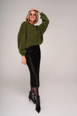 Attractive female model wearing trendy sweater, midi skirt and boots, posing on studio background.