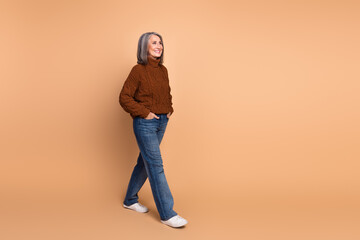 Stylish mature woman walking with confidence against beige background