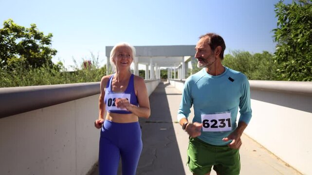 Elderly athletes wearing bib numbers are running a marathon together on a bridge on a beautiful sunny day, demonstrating their commitment to fitness and active lifestyle