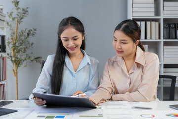 Fototapeta premium Two asian businesswomen reviewing financial documents and discussing data analysis in a bright, modern office environment
