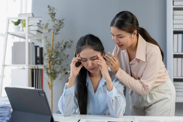 Two women in an office setting, one experiencing stress while the other offers comfort and support, fostering a caring workplace environment
