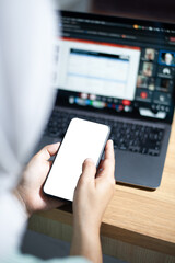 A person holding a smartphone in front of a laptop, engaged in digital communication or work.
