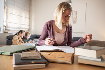 Obraz premium A mother works from home on her laptop in the living room, focused on her tasks, while her children play energetically in the background.