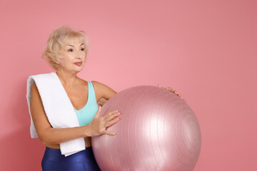 Senior woman with towel and fitness ball on pink background. Space for text