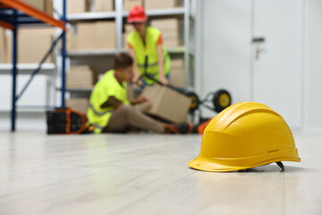 First aid. Hardhat on floor and woman helping her injured colleague in warehouse, selective focus