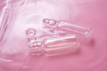 Ampoules in water on a pink background.