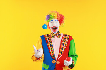 Emotional clown juggling balls on yellow background
