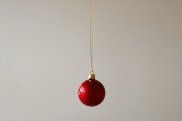 A single red Christmas ornament hangs from a gold string against a plain background.