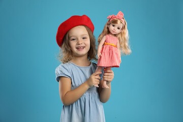 Cute little girl with doll on light blue background