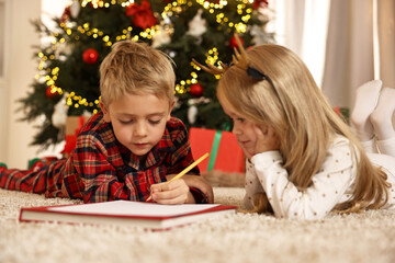 Little kids writing letter to Santa Claus on floor at home. Christmas celebration