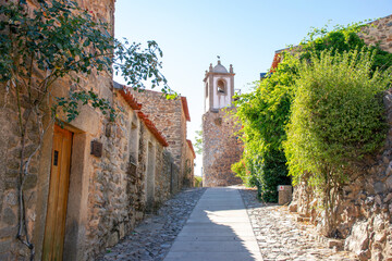 Old portuguese street in historic village with church tower at the end of the street. Urban european village. Vacation destination exploring. 