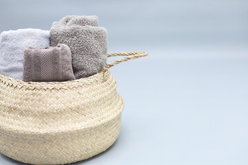 Straw wicker basket full of tolled cotton towels on grey background with copy space.