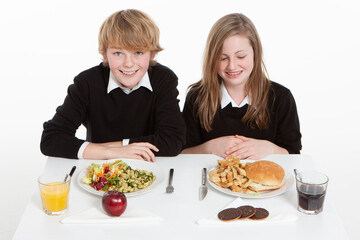 Early Teenage Students: Healthy Choice. An early teenage boy and girl with their contrasting school meals of salad and junk food.