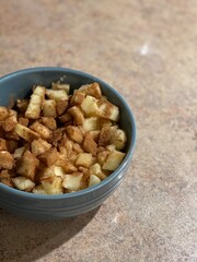 A close-up of diced apples seasoned with ground cinnamon, nutmeg, and brown sugar, placed in a blue bowl on a granite countertop, offering a warm and cozy culinary vibe.